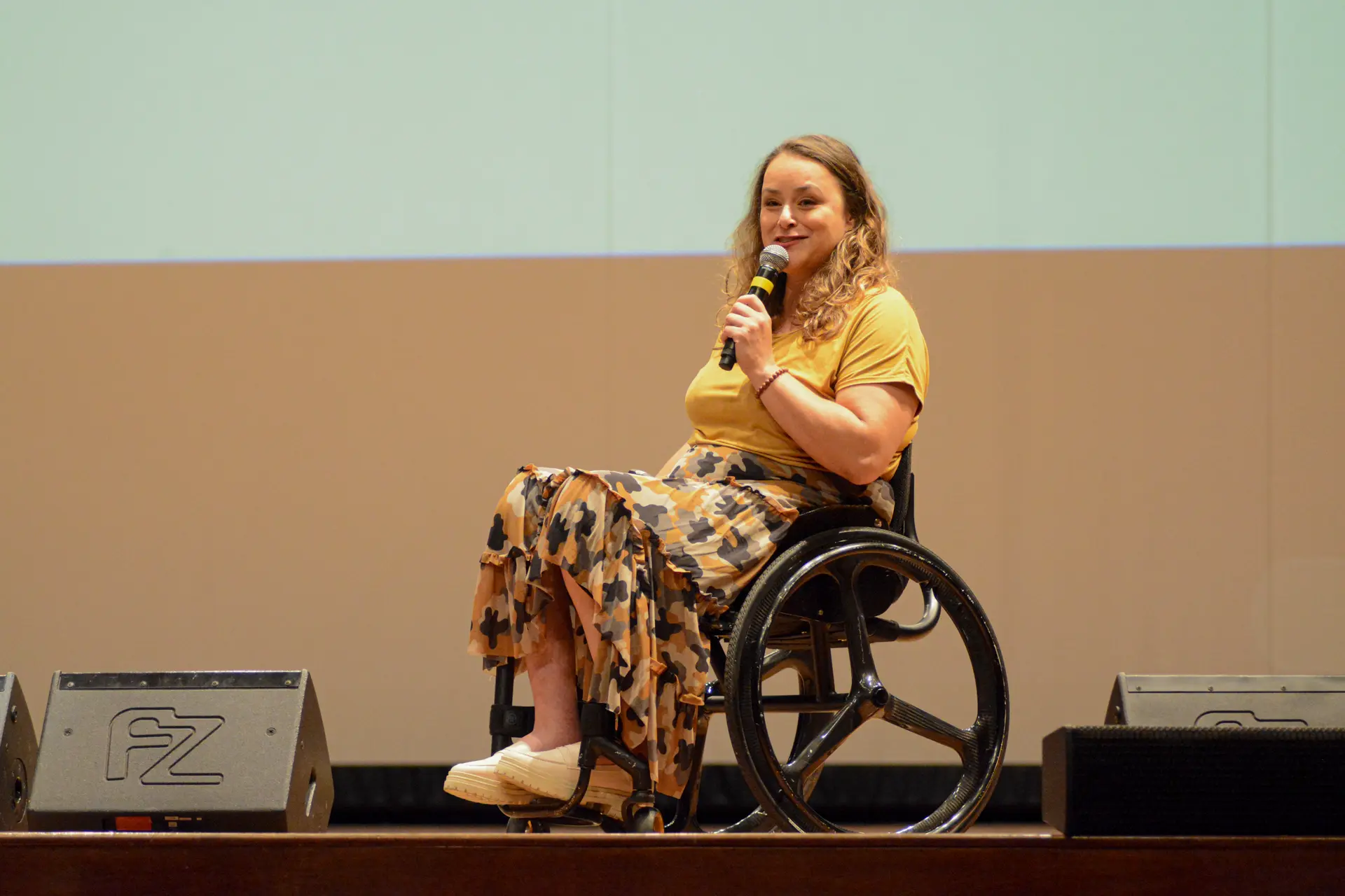 Palestrante em cadeira de rodas discursando em evento corporativo